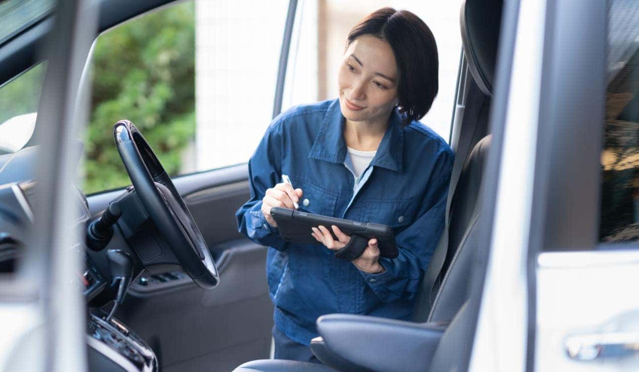 Automotive technician using a diagnostic tablet while inspecting the interior of a vehicle.