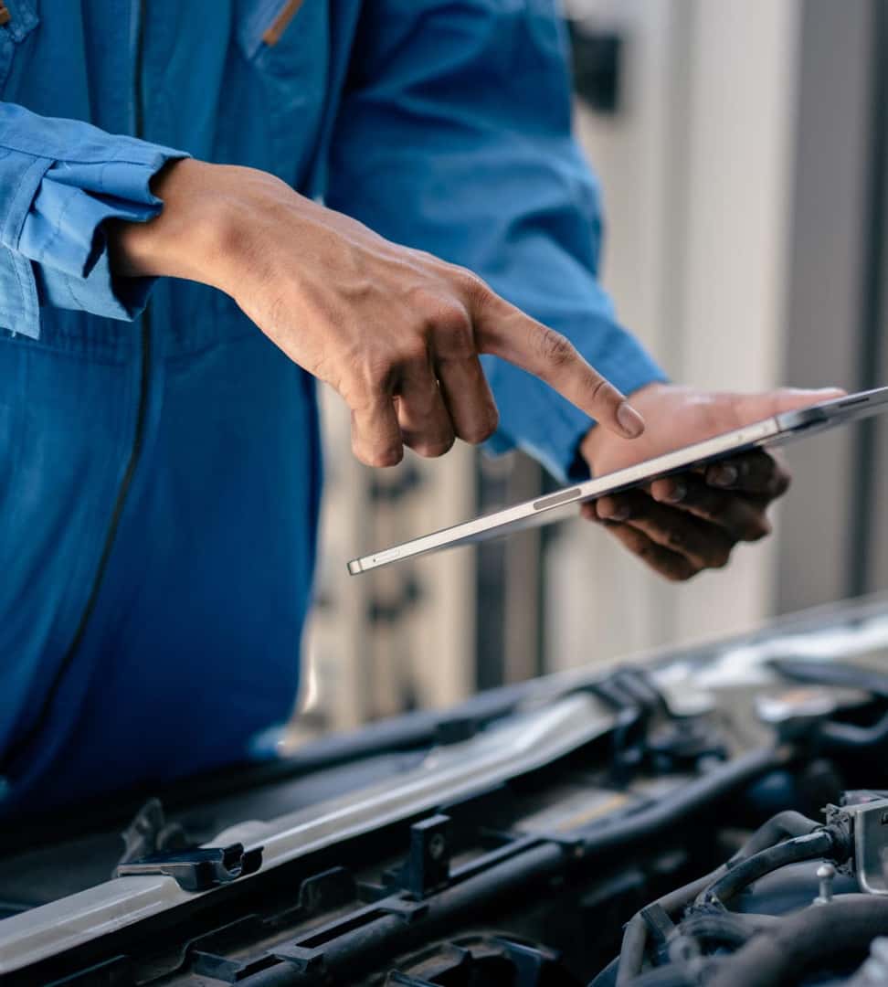Automotive technician using a tablet while inspecting a vehicle engine.