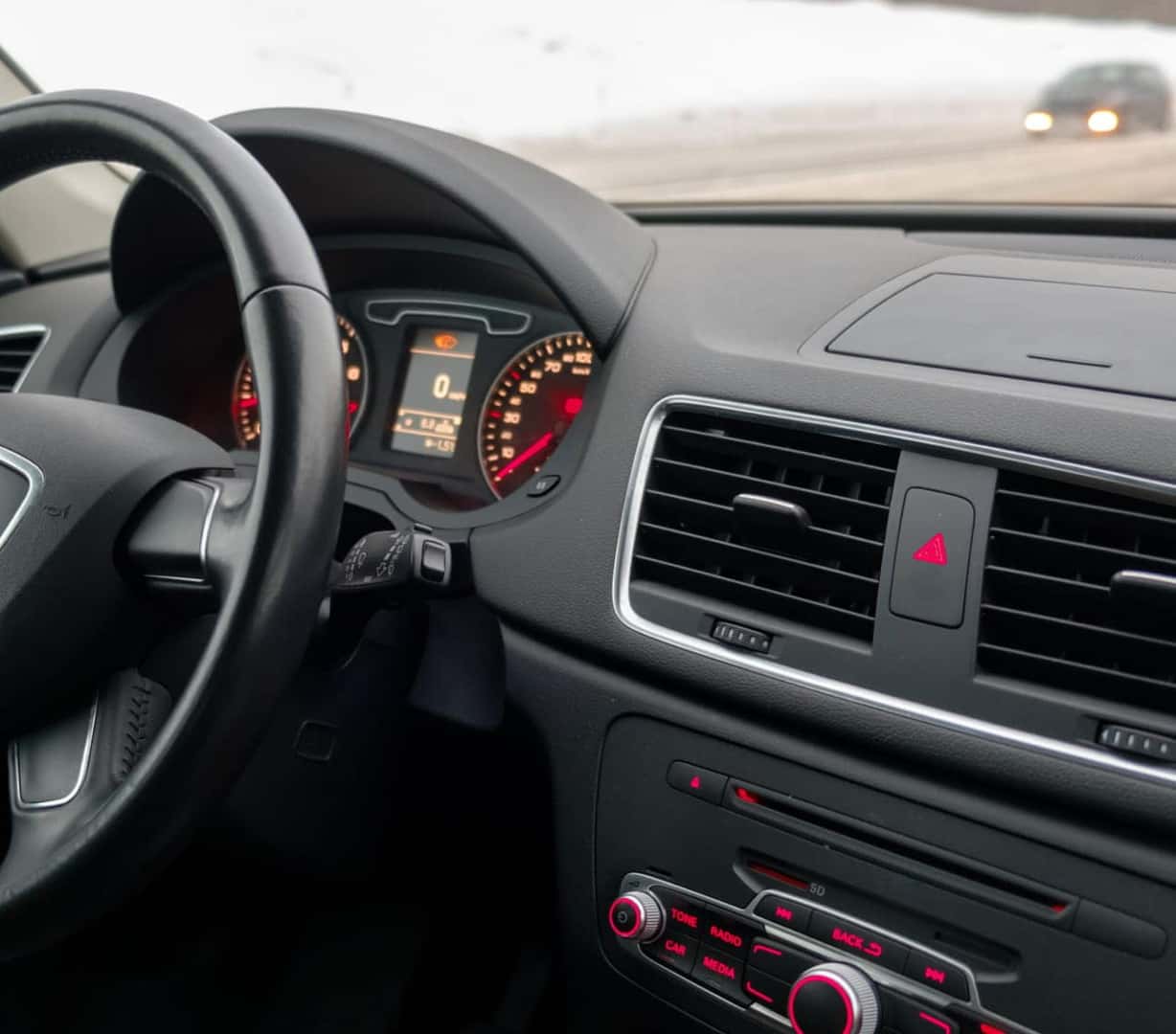 Vehicle interior with illuminated instrument cluster and dashboard controls while driving in snowy conditions.