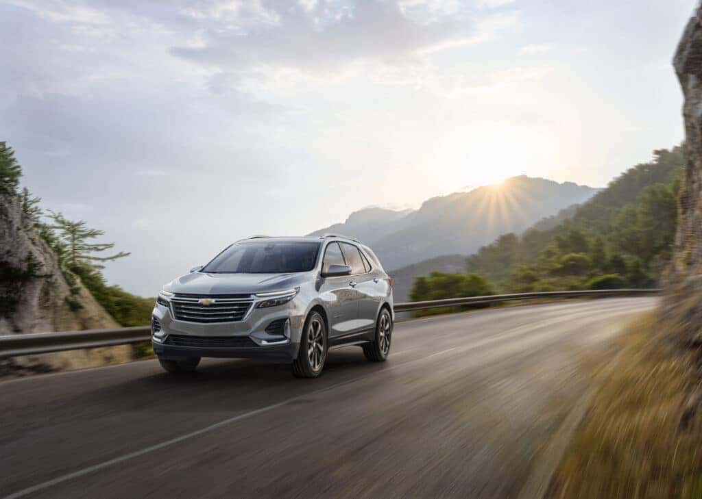 Front 3/4 view of Chevrolet Equinox Premier in Sterling Gray Metallic driving on mountain road.