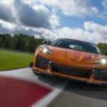 Front view of 2023 Chevrolet Corvette Z06 in Amplify Orange Tint driving on a track.