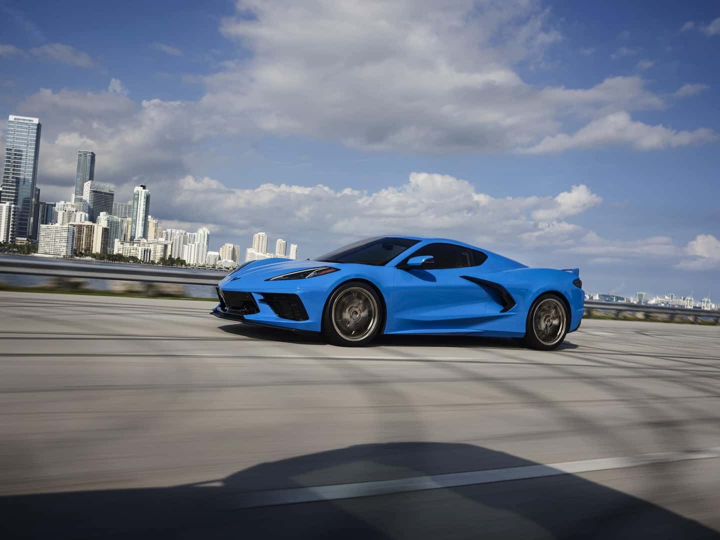 Side profile view of a 2024 Chevrolet Corvette Stingray in Rapid Blue driving over a bridge.