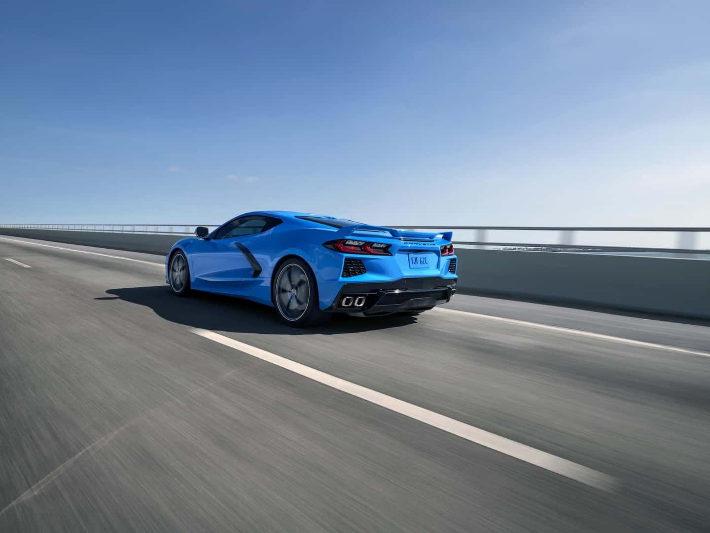 Rear 3/4 view of a 2024 Chevrolet Corvette Stingray in Rapid Blue driving over a bridge.