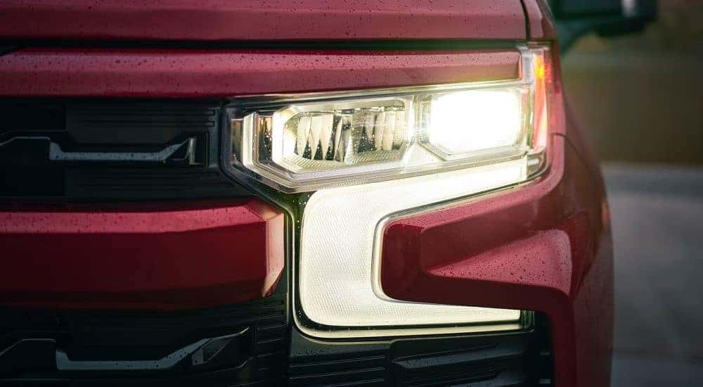 A close up shows the driver side headlight on a red 2023 Chevy Silverado 1500.