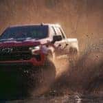 A red 2023 Chevy Silverado 1500 Z71 Trail Boss is shown kicking up mud after leaving a Chevy dealer.