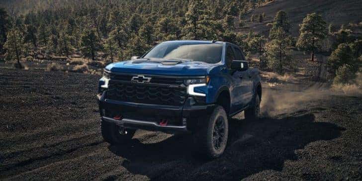 A blue 2023 Chevy Silverado ZR2 is shown driving up a trail after leaving a Chevy dealer.