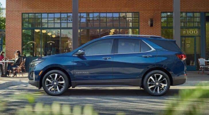 A blue 2023 Chevy Equinox is shown from the side in front of a brick building.