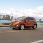 An orange 2015 Chevy Trax is shown driving on a city street after leaving a used Chevy dealership.