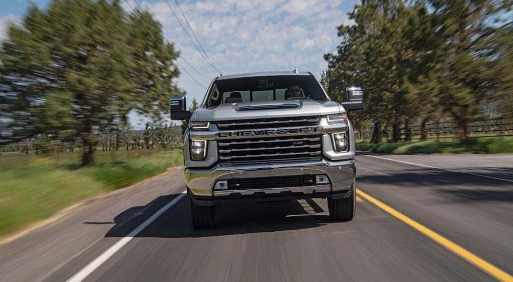 A silver 2020 Chevy Silverado 2500 HD Z71 is shown driving on a tree-lined road.