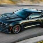 A black 2023 Chevy Camaro is shown driving on a road after visiting a Chevy dealer.