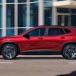 A red 2024 Chevy Trax is shown driving on a city road after visiting a Chevy dealer near Minden.