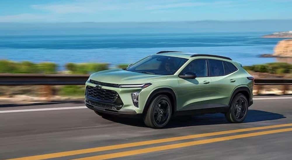 A green 2024 Chevy Trax is shown driving near an ocean.