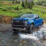 A blue 2023 Chevy Silverado ZR2 is shown driving through a creek.