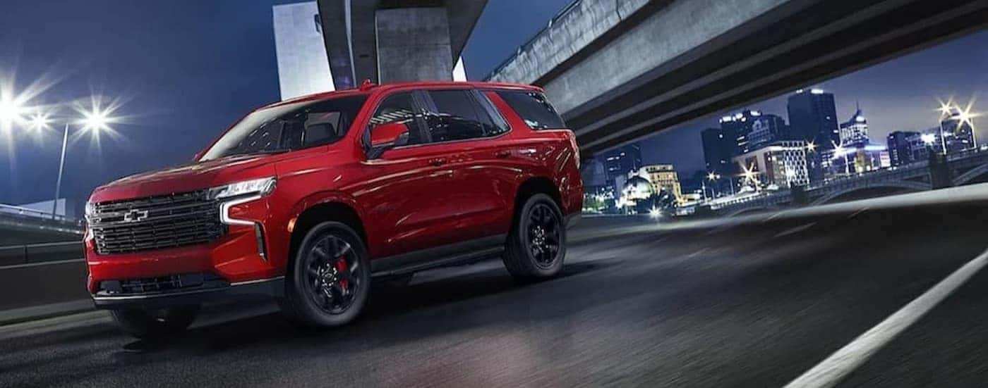 A red 2024 Chevy Tahoe is shown driving on a city street.