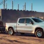 A white 2024 Chevy Silverado 1500 towing heavy machinery at a construction site.