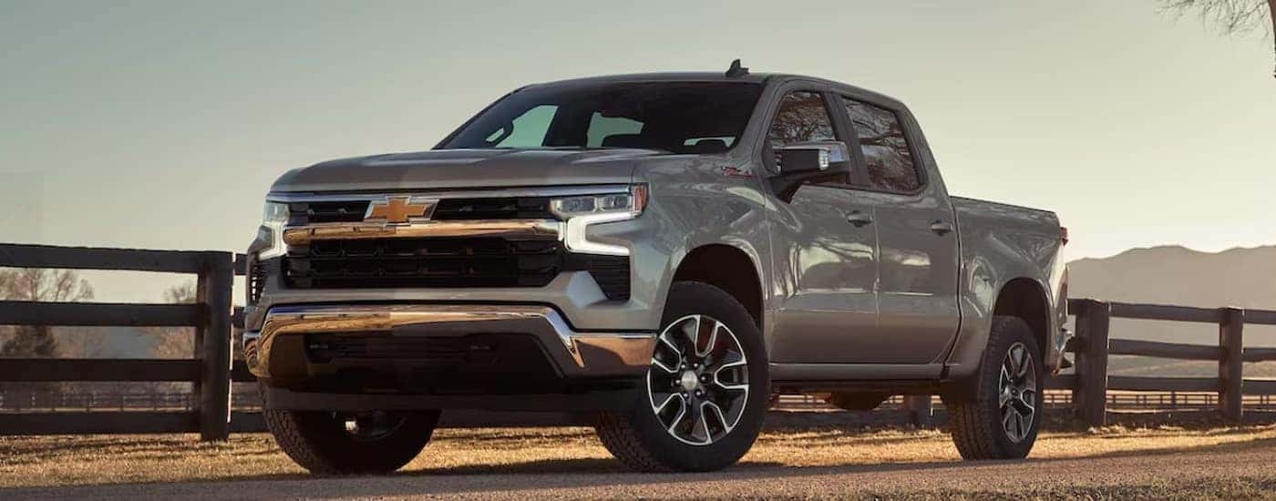 A silver 2024 Chevy Silverado 1500 LT Z71 is shown parked next to a wooden fence.