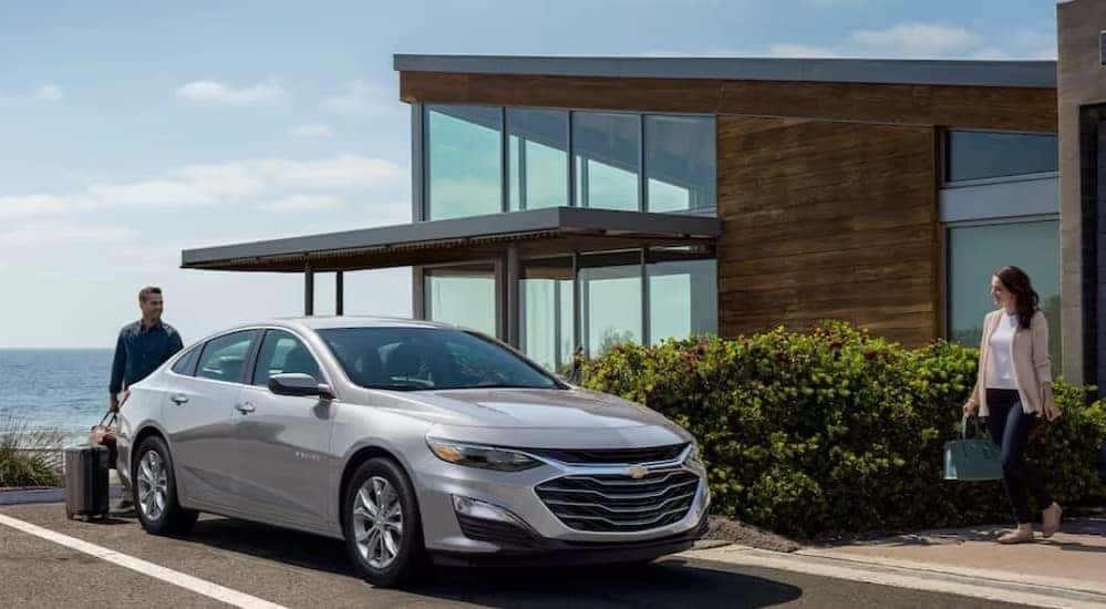 A silver 2024 Chevy Malibu for sale is shown parked near an ocean.