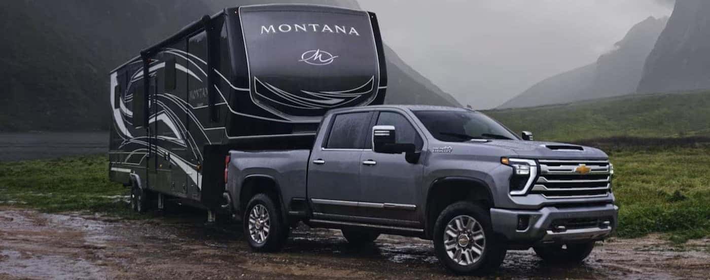 A gray 2024 Chevy Silverado 2500 HD is shown parked while towing a trailer.