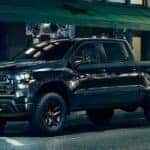 A black 2024 Chevy Silverado 1500 Midnight Trailboss Z71 is shown parked on a city street.