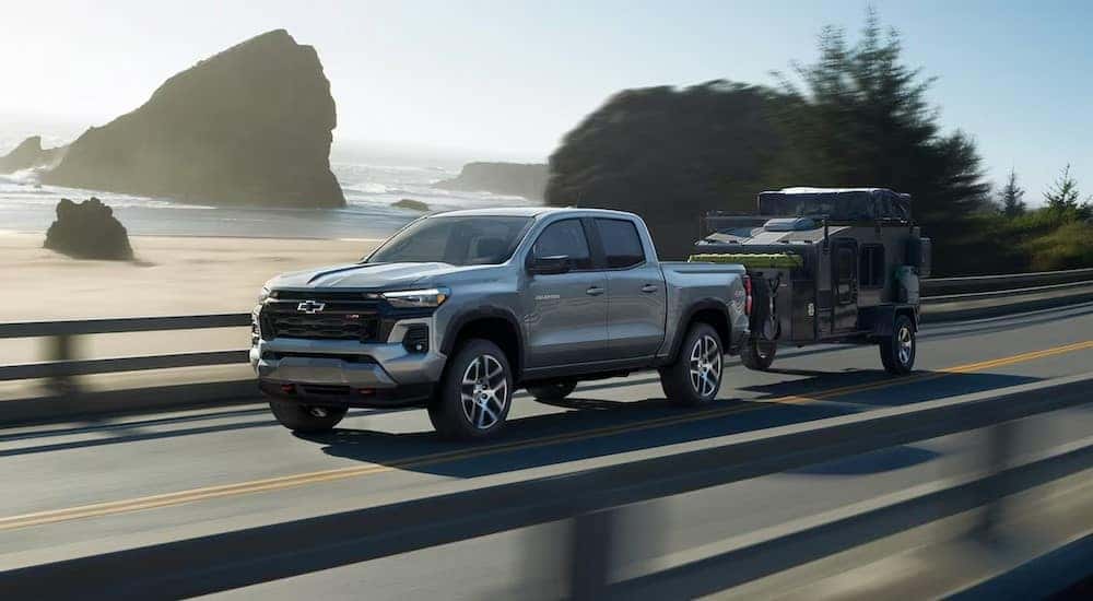 A silver 2024 Chevy Colorado Z71 is shown towing a trailer near an ocean after viewing trucks for sale.