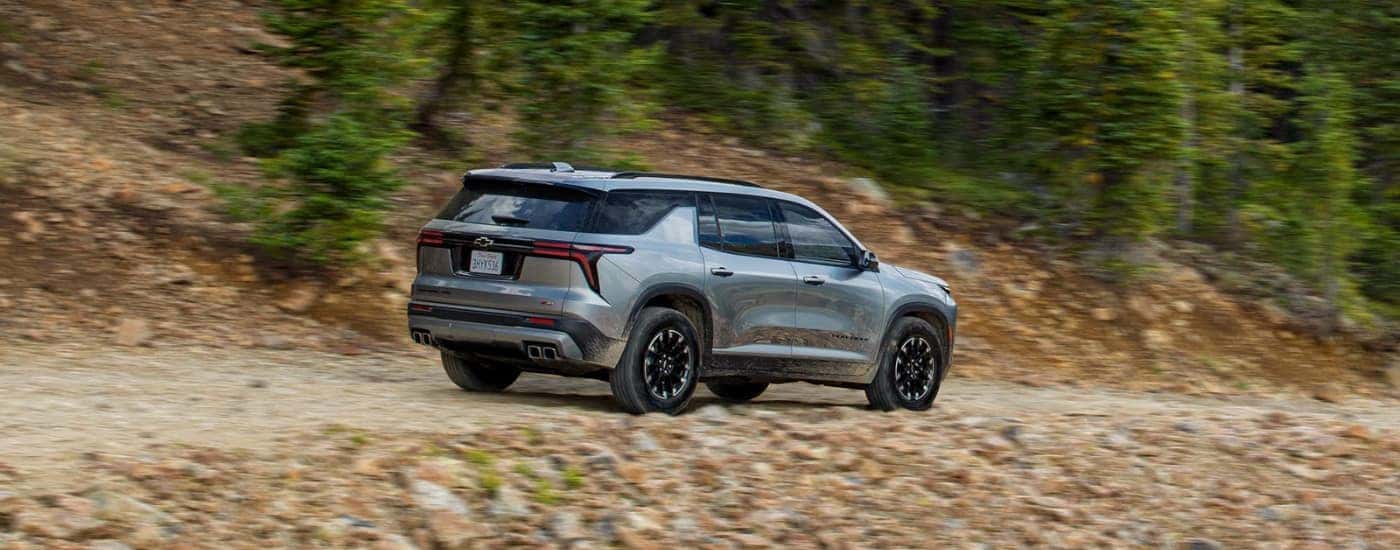 A grey 2024 Chevy Traverse Z71 is shown driving on a tree-lined road.