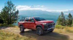 A red 2024 Chevy Colorado Trail Boss is shown driving on a dirt road.