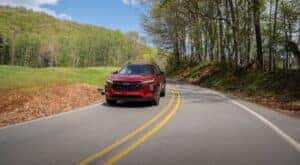 A red 2024 Chevy Trax RS driving on a tree-lined road.