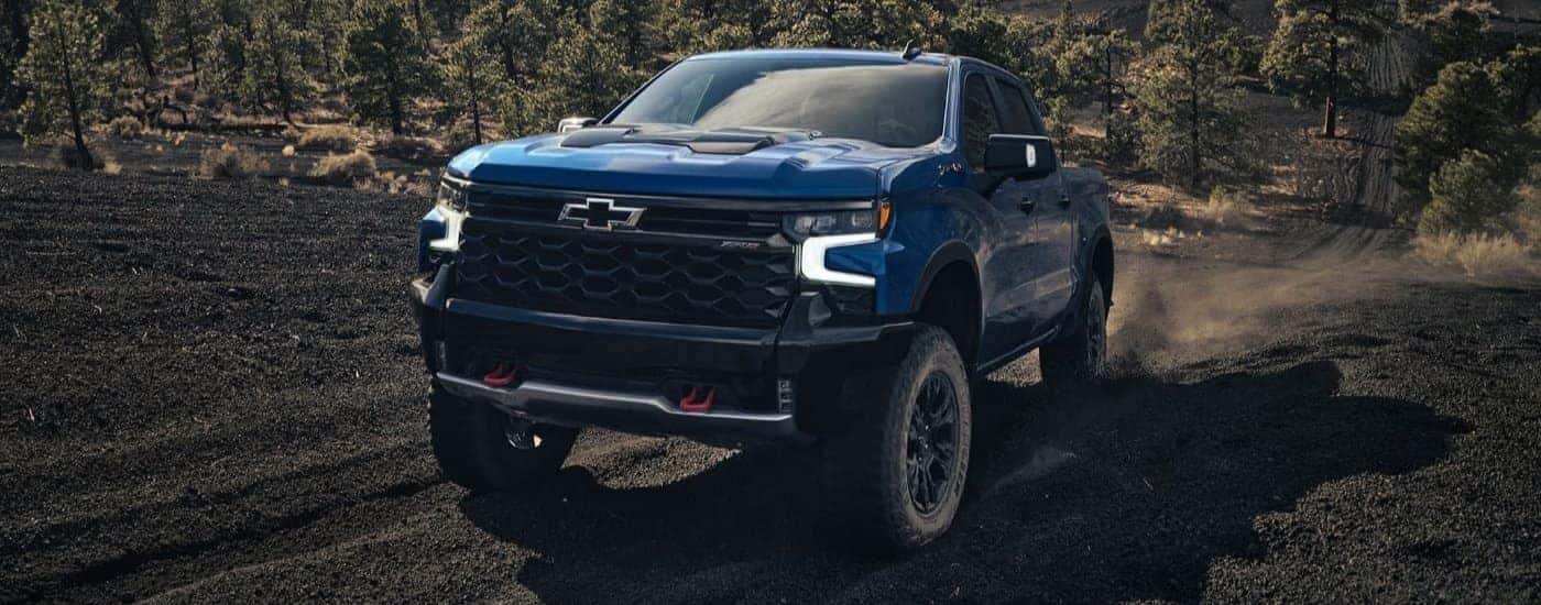 A blue 2023 Chevy Silverado ZR2 is shown driving up a trail after leaving a Chevy dealer.