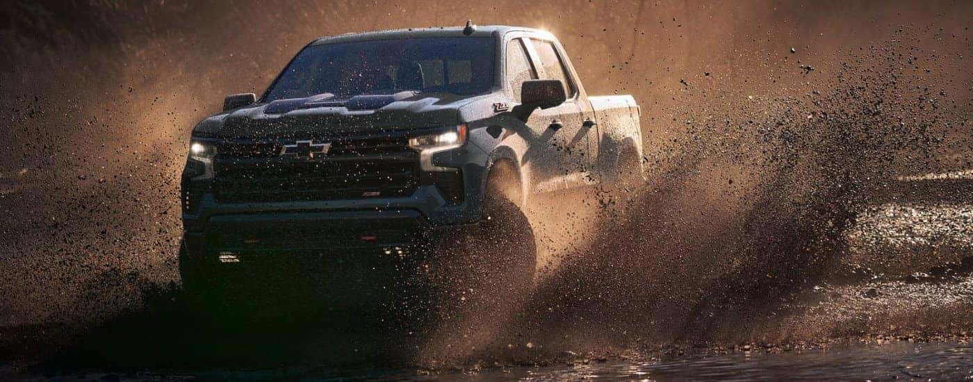 A black 2025 Chevy Silverado 1500 Z71 kicking up mud off-road.