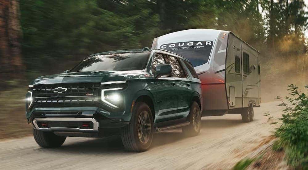A green 2026 Chevy Tahoe Z71 towing a camper.