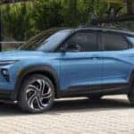 Blue 2026 Chevy Trailblazer RS parked in front of a reflective glass window in the city.