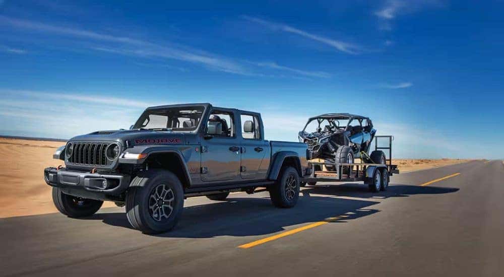 A grey 2024 Jeep Gladiator Mojave towing an ATV through a desert.