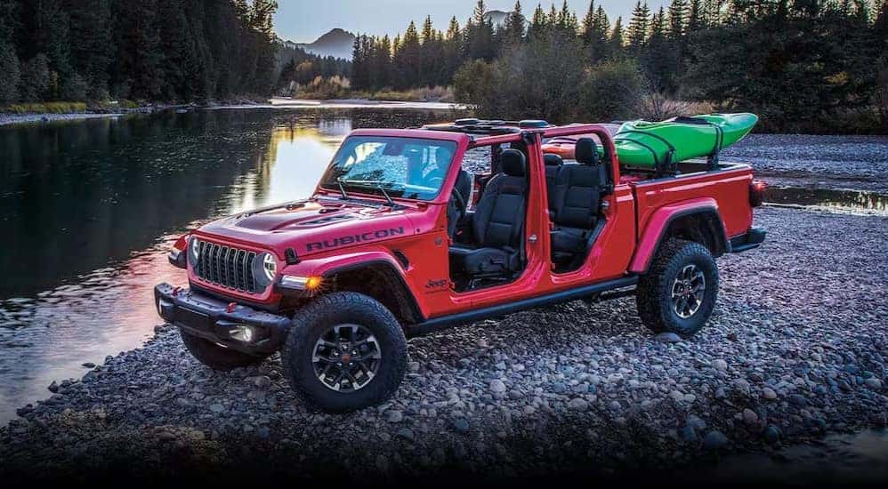 A red 2024 Jeep Gladiator Rubicon is shown parked off-road near a pond.