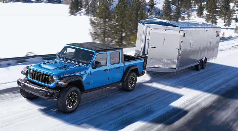A blue 2024 Jeep Gladiator Rubicon towing a trailer over a snowy road.