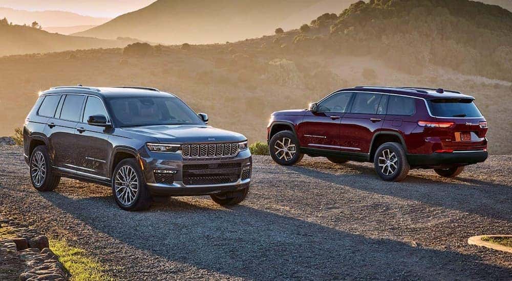 A grey 2025 Jeep Grand Cherokee Summit and red 2025 Grand Cherokee Limited parked outside at sunset.