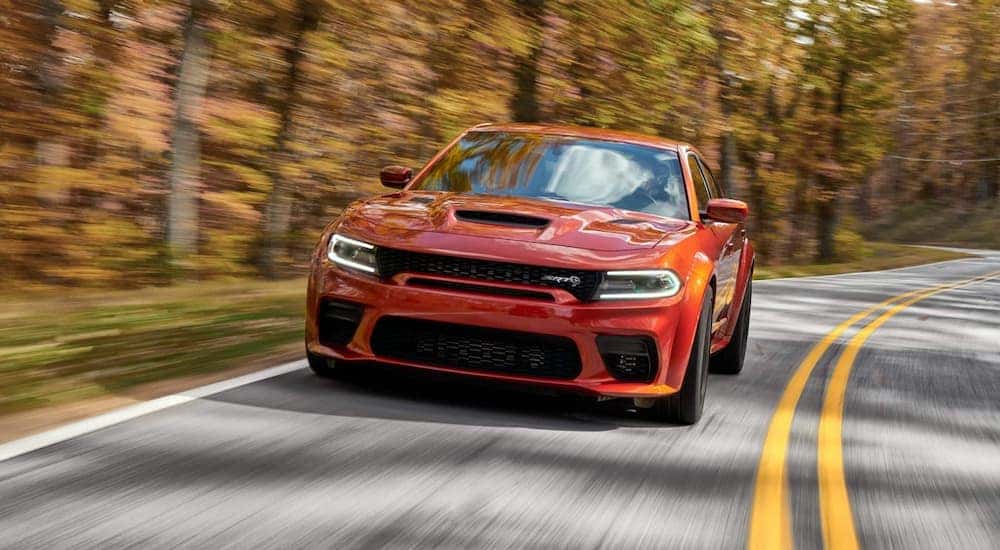 A orange 2023 Dodge Charger SRT Hellcat driving through a forest.