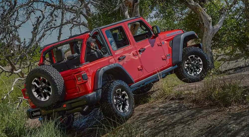 A red 2025 Jeep Wrangler is off-roading on a steep trail.
