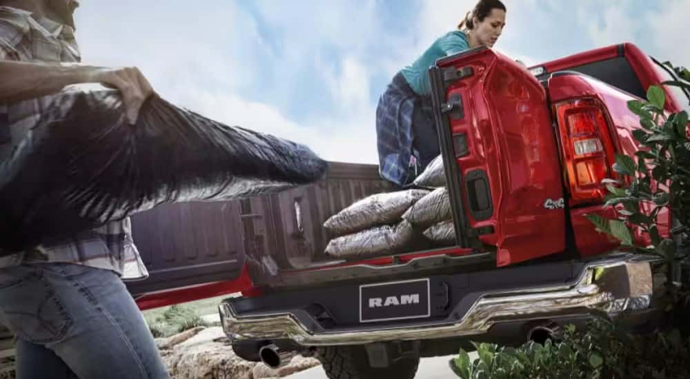 The multifunctional tailgate is shown open on a red 2025 Ram 1500 as people load bags of soil.