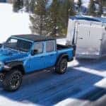 A blue 2025 Jeep Gladiator Rubicon towing a trailer down a snowy road.
