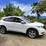 Side view of a white 2022 Honda HR-V sitting on a driveway with a beach view in the background
