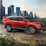 a red 2022 honda cr-v hybrid driving on a road with a city view in the background