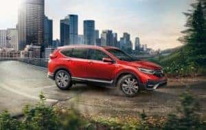 a red 2022 honda cr-v hybrid driving on a road with a city view in the background