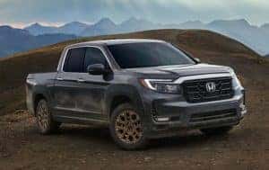 A grey 2023 Honda Ridgeline driving off road with mountains in the background