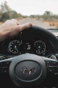A person holding a black Hyundai steering wheel with one hand