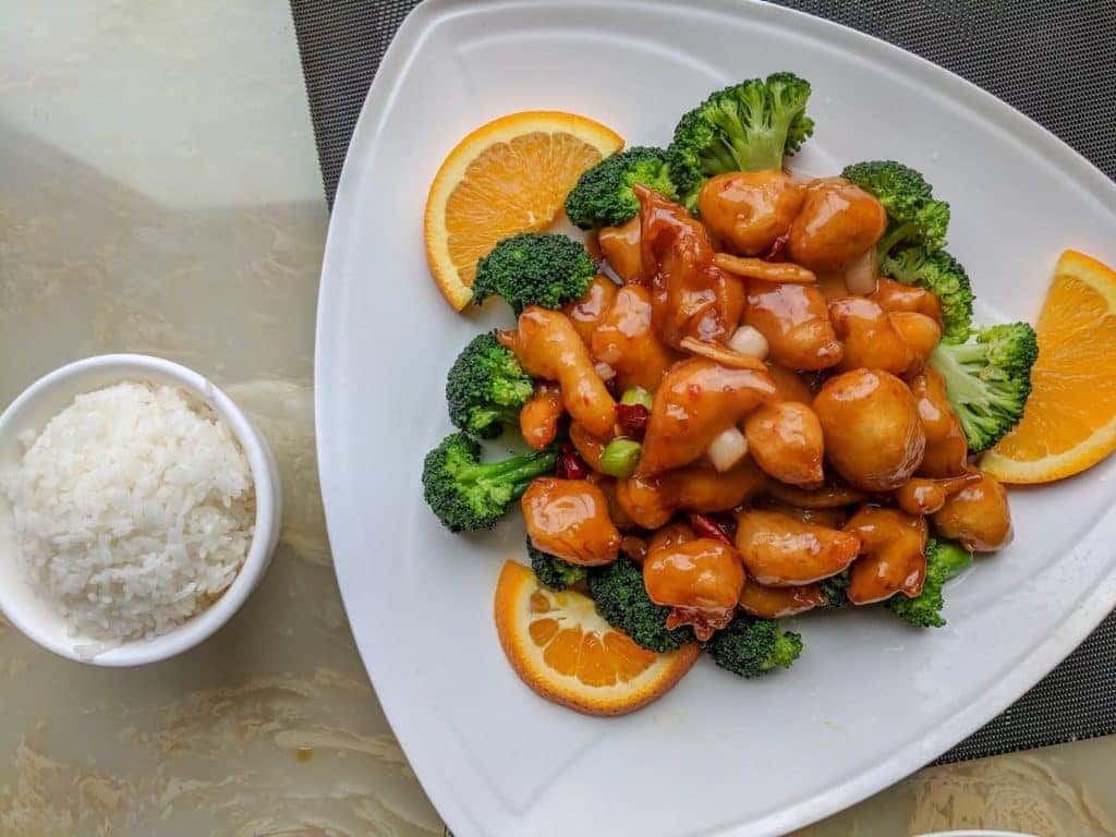 Orange chinese chicken and broccoli sitting on a plate at a restaurant table