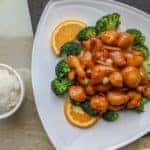 Orange chinese chicken and broccoli sitting on a plate at a restaurant table