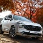 A white Hyundai SUV driving on a road with Autumn trees in the background