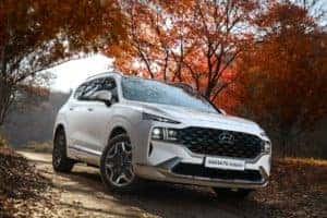 A white Hyundai SUV driving on a road with Autumn trees in the background