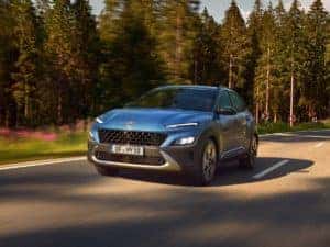 A blue Hyundai Kona driving in a forest setting