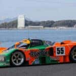 Orange, Green Mazda 787B race Car Water Buildings Mountains